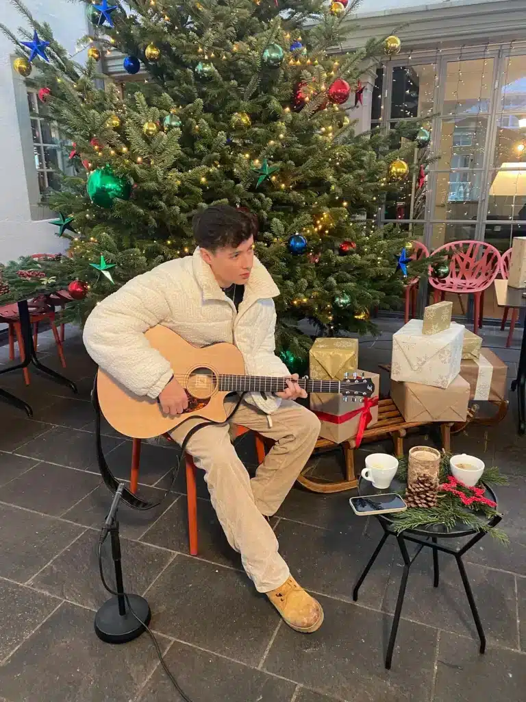 a man sitting in a chair playing a guitar next to a christmas tree